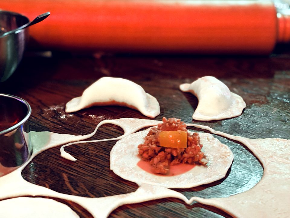 Chicken empanadas being filled and folded by hand, with a rolling pin behind